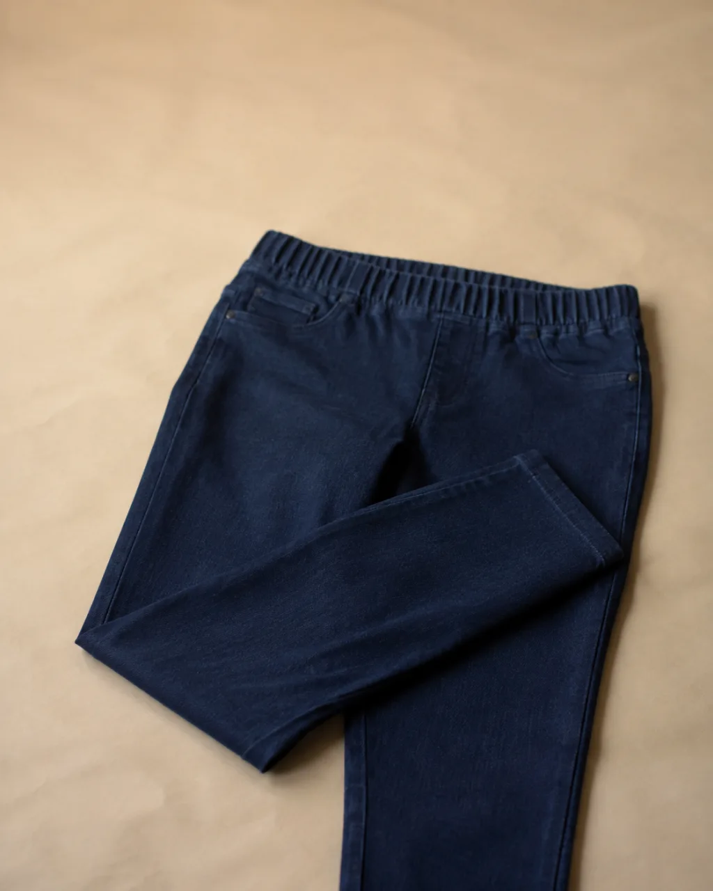 a pair of jeggings laid flat with one leg folded back across the other with a mid rise and a full elastic waistband , fabric: Cotton/rayon/polyester/Lycra blend