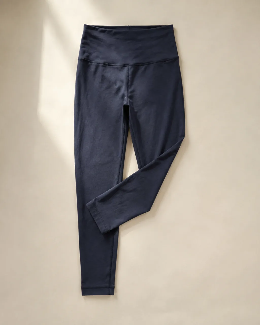 a pair of leggings laid flat with one leg folded back across the other with a high rise and a full elastic waistband